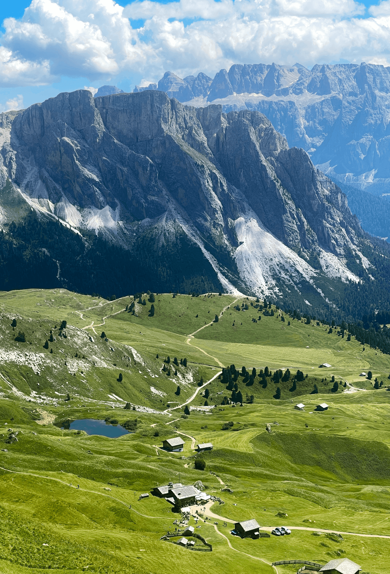 Panoramic view of the Dolomites valley with green meadows and mountain huts
